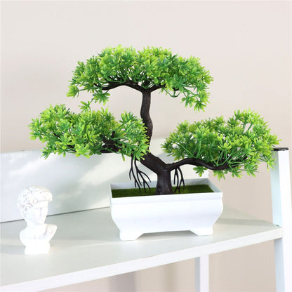 Artificial bonsai tree with dense, vibrant green foliage and a curved black trunk, set in a rectangular white ceramic pot and displayed on a white shelf beside a small decorative bust—ideal for minimalist decor, indoor greenery, or modern home accents.