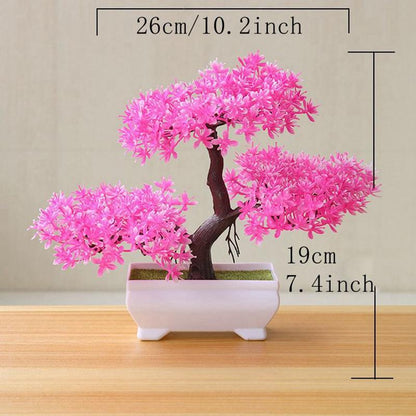 Medium-sized artificial pink blossom bonsai tree in a white ceramic pot, measuring 10.2 inches wide and 7.4 inches tall, displayed on a wooden surface with clear size dimensions—perfect for desk décor, shelf styling, or home office accents.
