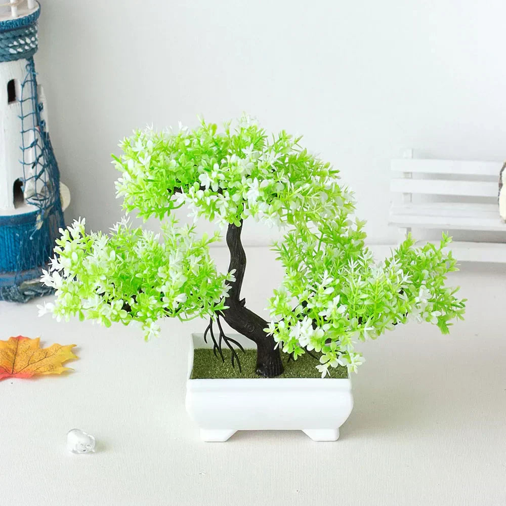 Artificial green blossom bonsai tree with a black curved trunk and dense white-green foliage, placed in a white ceramic pot on a tabletop with nautical and fall-themed decorations—ideal for small space décor, shelf styling, or zen-inspired home accents.